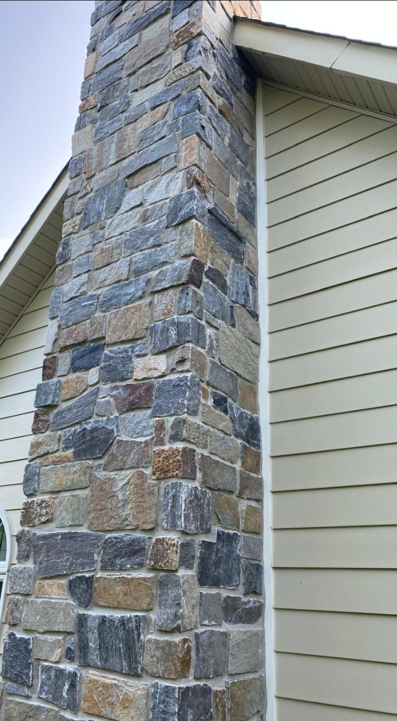 Completed grey stone veneer wall beneath exterior siding and window trim