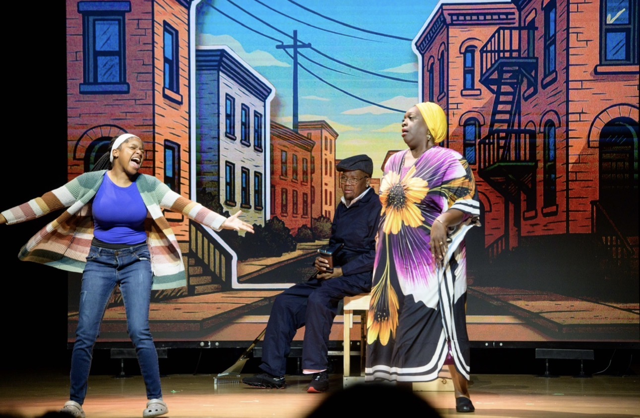 Three performers on a brownstone stoop, one in a sunflower dress, mid-scene