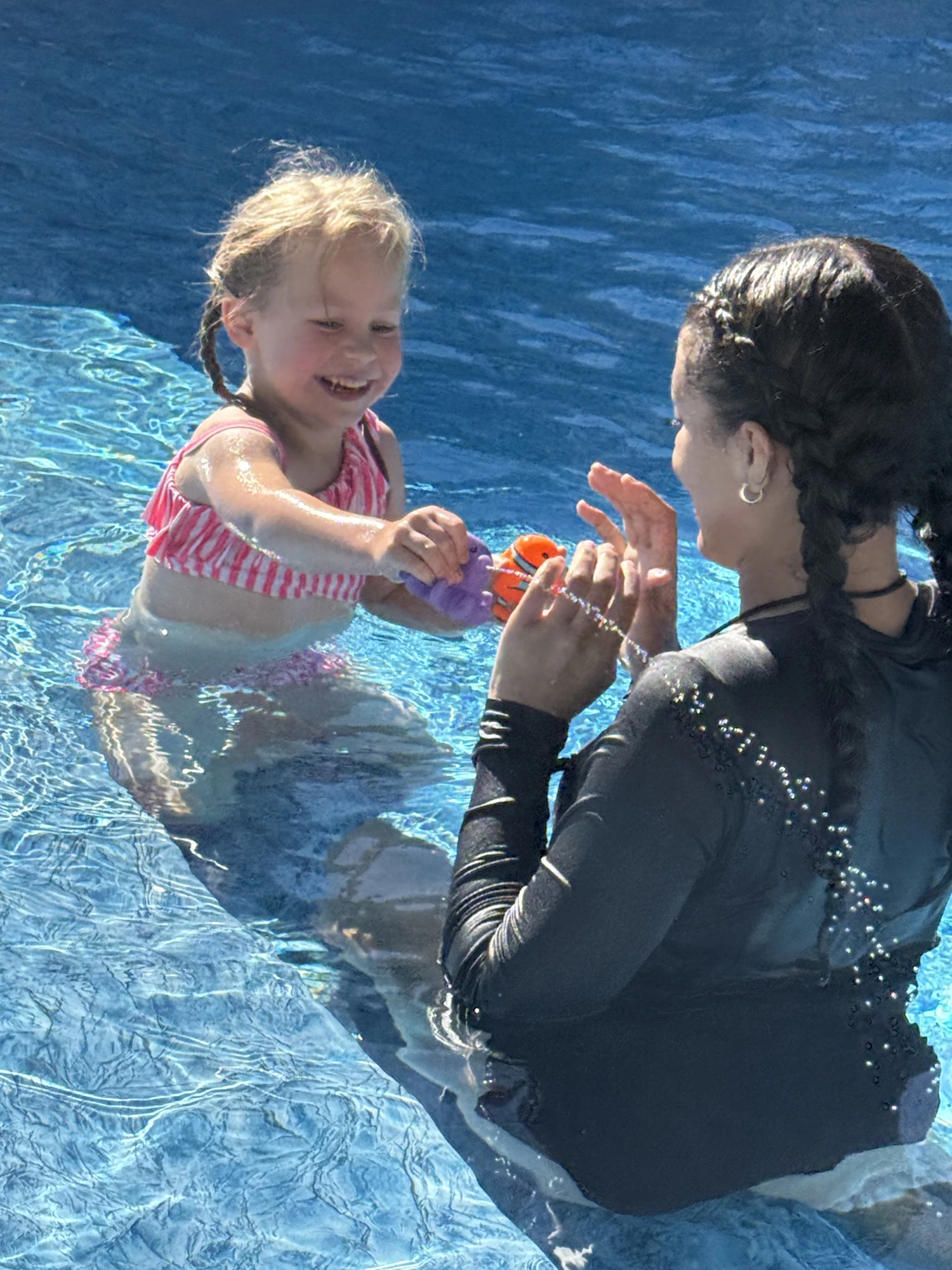 Coach playing with a joyful young swimmer in the pool
